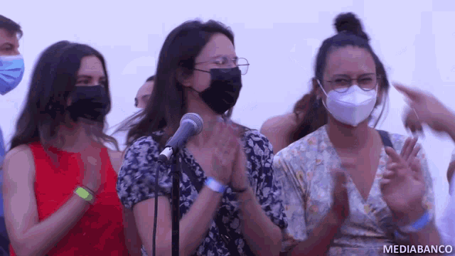 a group of people wearing face masks are clapping in front of a microphone with mediabanco written on the bottom