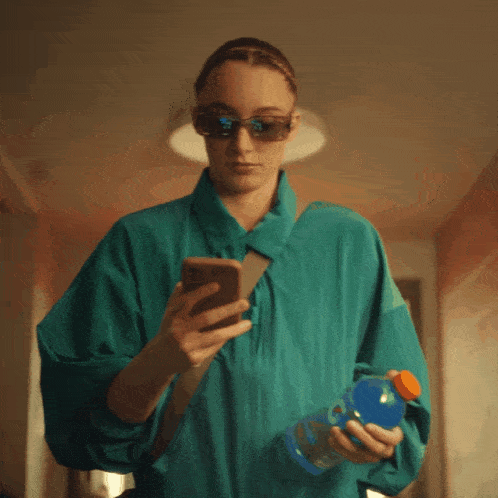 a woman holding a bottle of gatorade and looking at her phone