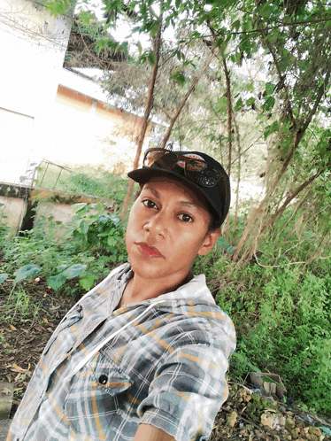 a man wearing a plaid shirt and a hat takes a picture