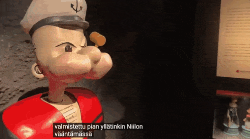 a statue of popeye is standing in front of a sign that says valmistettu pian yliatinkin niilon vaantamassa