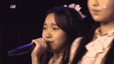 a girl singing into a microphone with the word live in the background