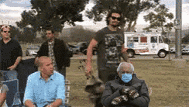 a man wearing a face mask is sitting in a park with other people