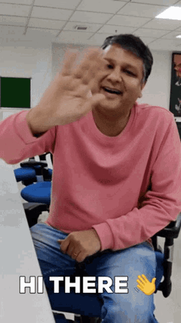 a man in a pink shirt is sitting on a blue chair and waving with the words hi there below him