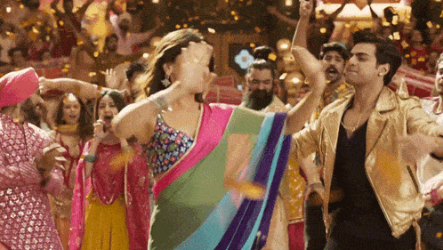 a woman in a sari is dancing with a man in a gold jacket in front of a crowd of people