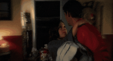a man in a red shirt is holding a woman in a dark room