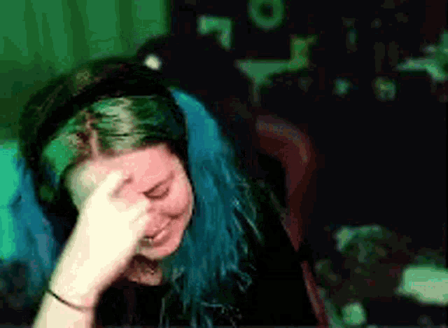 a woman with blue hair is wearing headphones and covering her face with her hand