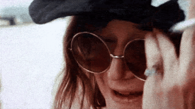 a woman wearing sunglasses and a hat is covering her face with her hand