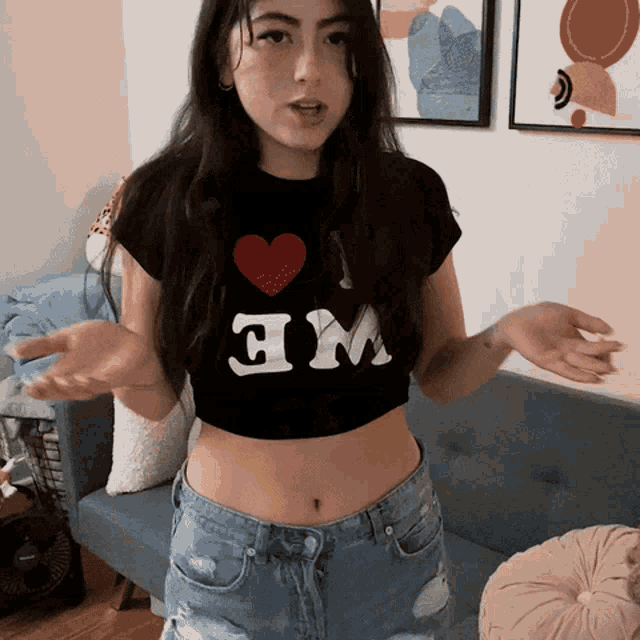 a woman wearing a crop top that says i 'm standing in front of a couch