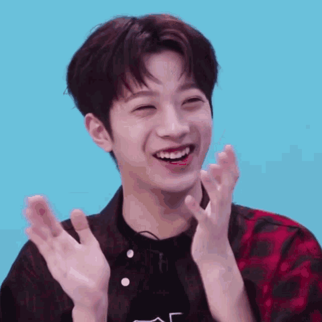 a young man in a plaid shirt is clapping his hands and smiling
