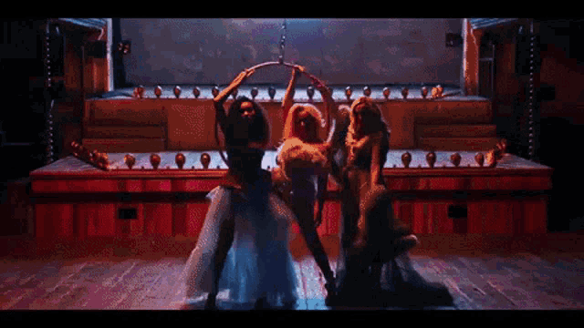 three women are dancing on a stage with a hoop around their heads