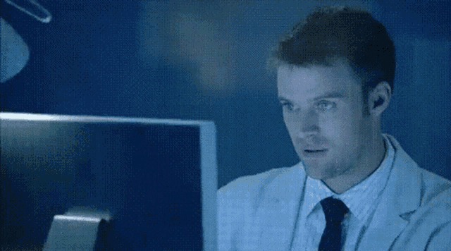 a man in a lab coat is giving a thumbs up in front of a computer monitor