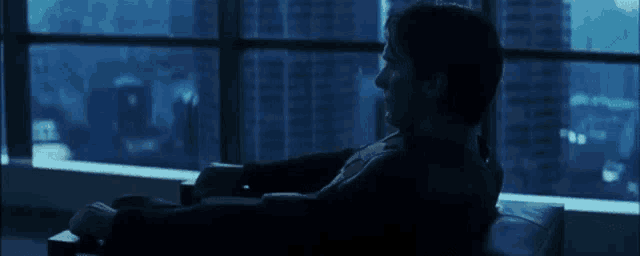 a man in a suit is sitting in front of a window looking out .