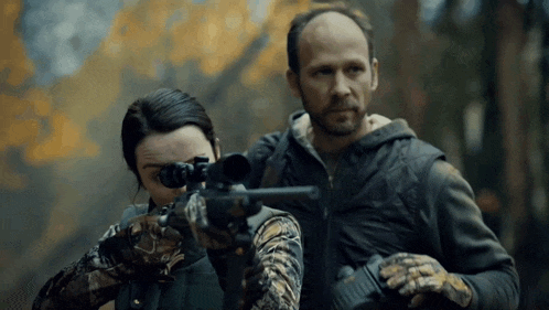 a man and a woman are holding guns in a forest ..