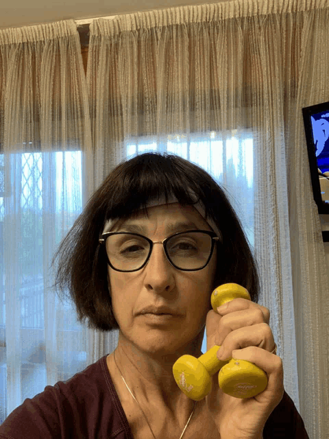 a woman wearing glasses and a headband is holding a pair of yellow dumbbells in her hands