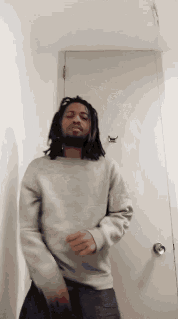 a man with dreadlocks and a beard is dancing in front of a white door .