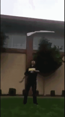 a man throwing a frisbee in front of a building that says ' ucsd ' on his shirt