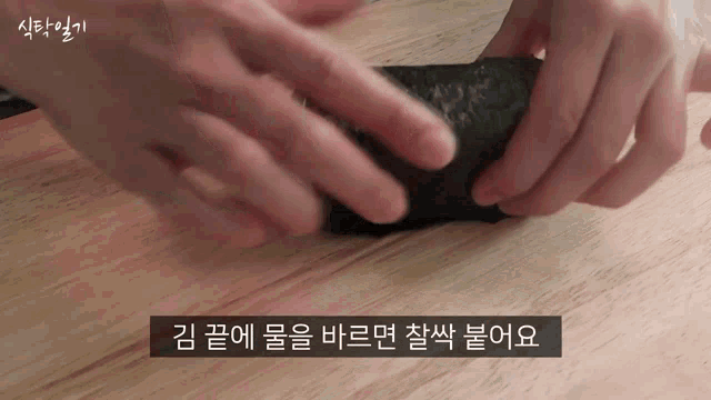 a person is holding a piece of food on a wooden table with korean writing on it