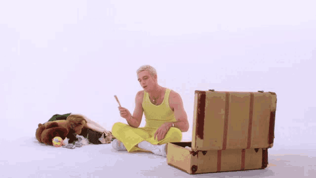 a man in a yellow tank top is sitting on the floor next to a trunk