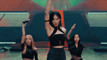 a woman in a black top is dancing on a stage with two other women