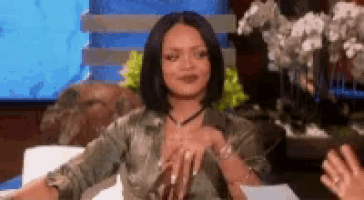 a woman is sitting on a couch with her hands on her chest and talking to someone .