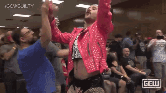 a wrestler in a red jacket is standing in front of a crowd .