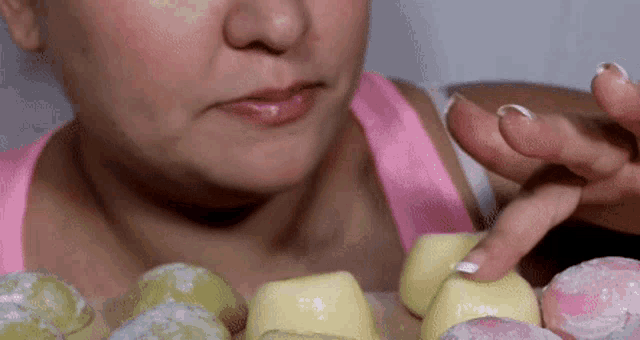 a woman in a pink tank top is eating a variety of desserts with her finger .