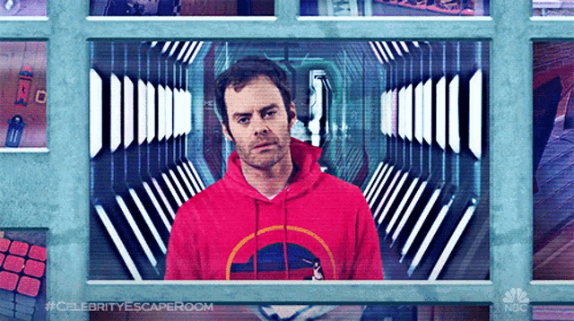 a man in a red hoodie is standing in front of a screen that says #celebrityescaperoom
