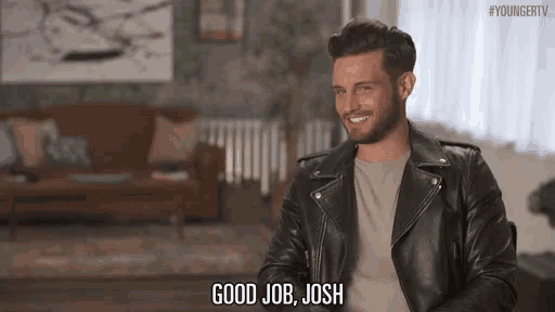 a man in a leather jacket is sitting on a couch in a living room .
