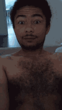 a shirtless man with a beard looks at the camera with his eyes closed