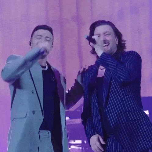 two men in suits are singing into microphones