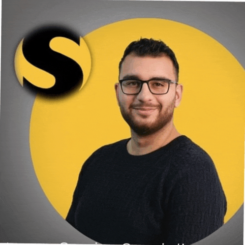 a man wearing glasses stands in front of a yellow circle with the letter s in the middle