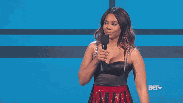 a woman in a black top and red skirt is holding a microphone in front of a bet logo