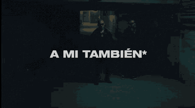 two men standing in a dark room with the words " a mi tambien " on the screen