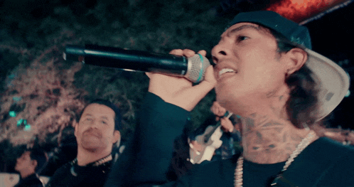 a man is singing into a microphone with a tattoo on his neck