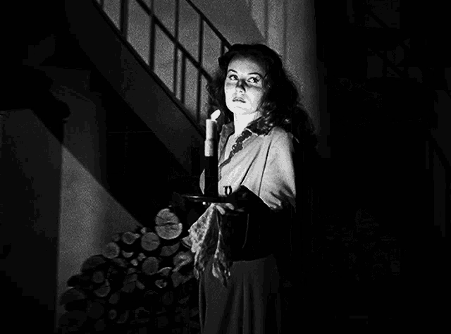 a black and white photo of a woman holding a candle in front of a staircase
