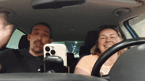 a man and a woman are sitting in a car with a cell phone in the back seat