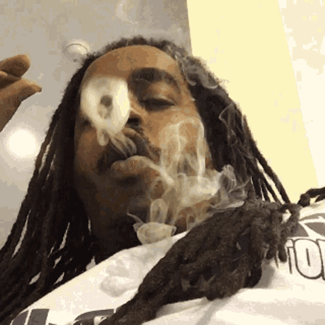 a man with dreadlocks is smoking a cigarette while wearing a shirt with the letter t on it