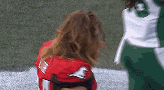 a cheerleader in a red jersey is kneeling down on the field .