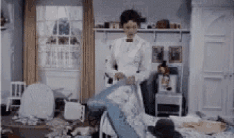 a woman in a white dress is standing in a messy bedroom .