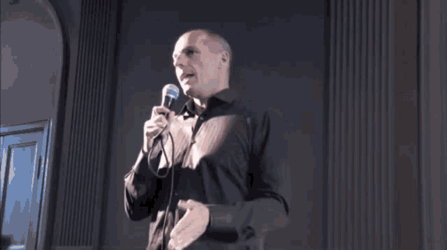 a bald man is holding a microphone and giving the middle finger