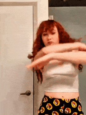 a woman with red hair is standing in front of a door wearing a white crop top and black shorts .