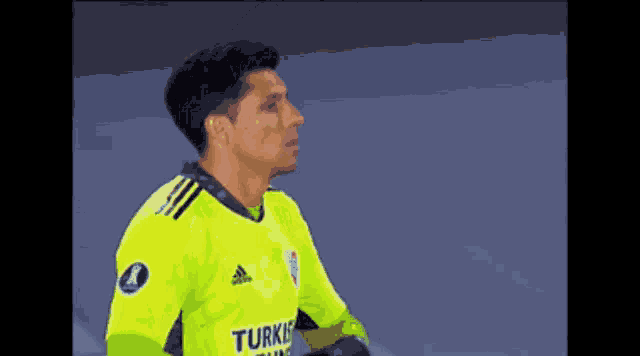 a soccer player wearing a yellow adidas jersey is standing on the field .