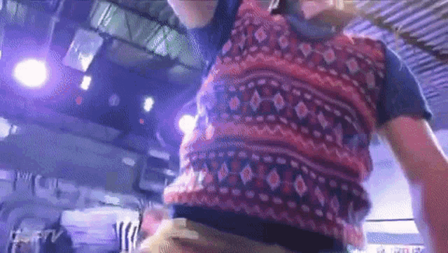 a person wearing a vest with a pattern on it is dancing in a room with purple lights .
