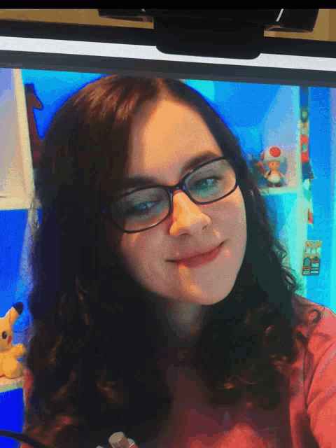 a girl wearing glasses is smiling in front of a blue screen