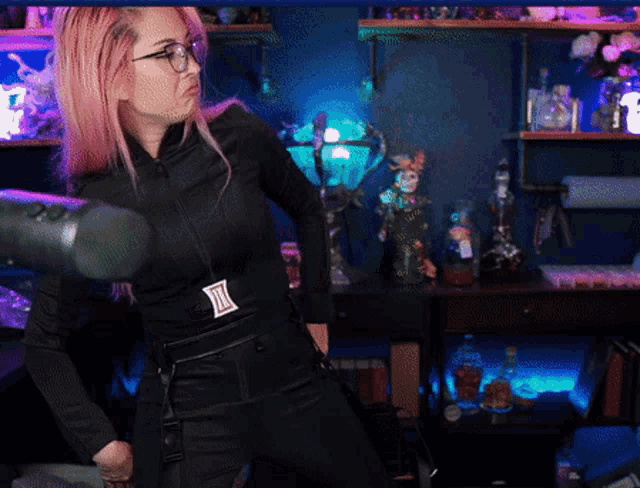 a woman with pink hair and glasses is wearing a black outfit with a belt that says ' i ' on it