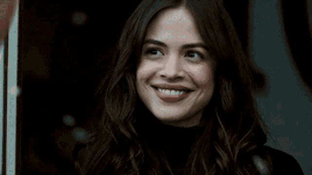 a woman with long dark hair is smiling while wearing a black turtleneck sweater .