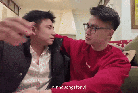 two men are sitting on a couch and one of them is wearing a red sweater that says " ninhduongstoryl "