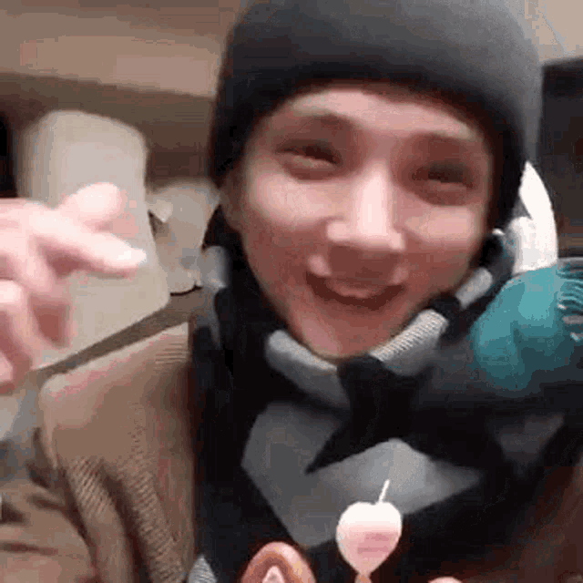 a man wearing a beanie and scarf is holding a cake with a heart shaped candle on it .