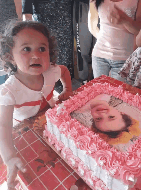 a little girl stands in front of a cake with a picture of a girl on it