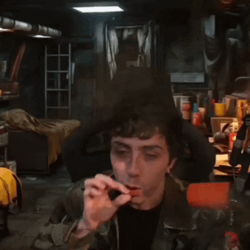 a man smoking a cigarette in a dark room with a ladder in the background